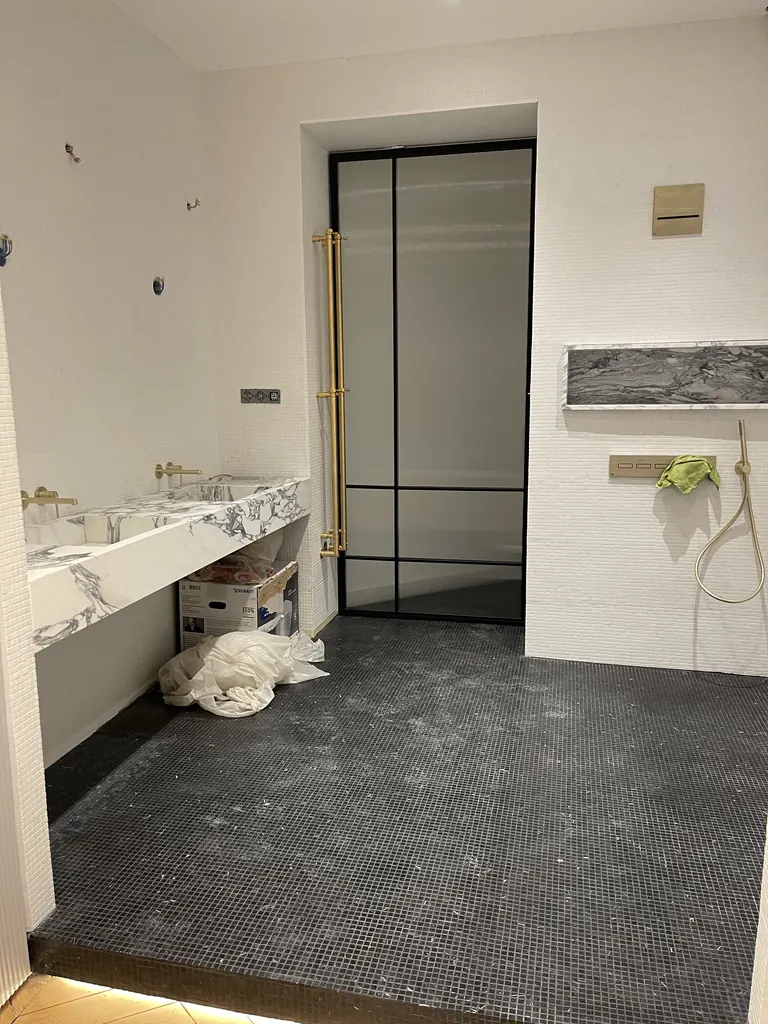 Salle de bain en travaux avec vasque veinée, robinetterie laiton et mosaïque sombre