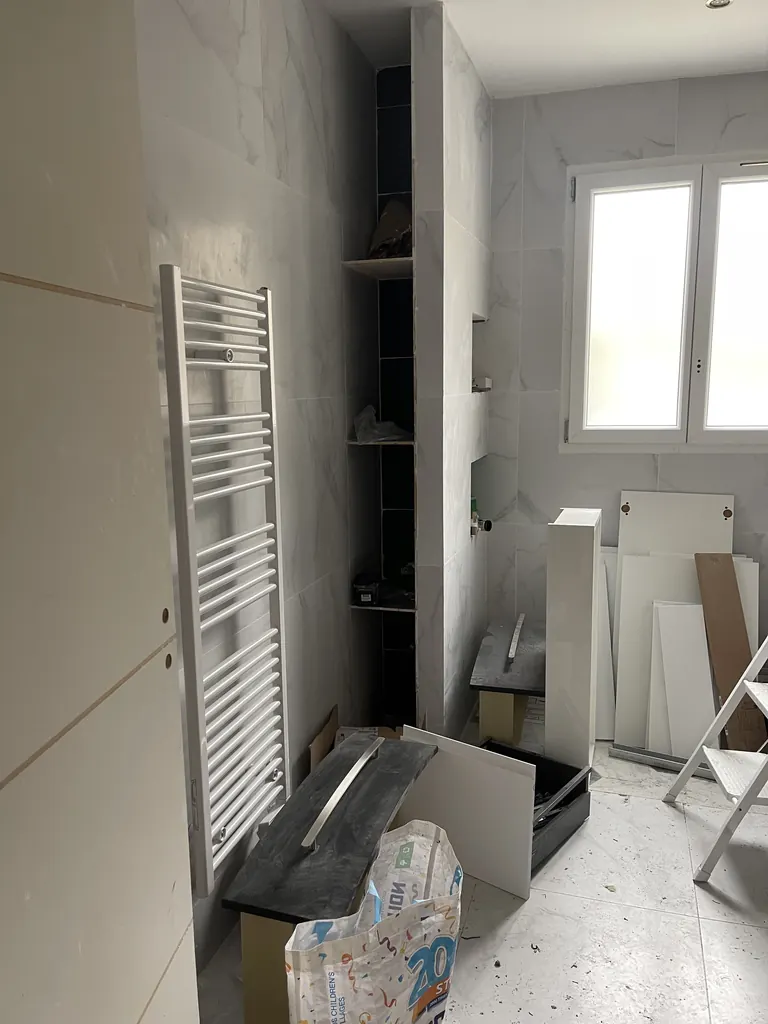Salle de bain en travaux avec carrelage mural, sèche-serviettes et niche