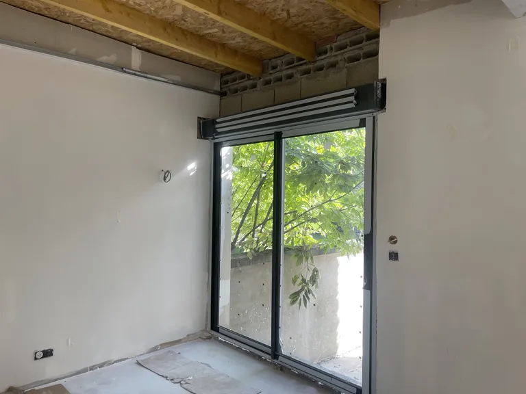 Baie vitrée coulissante avec coffre de volet roulant, solives et panneaux OSB apparents sur un chantier