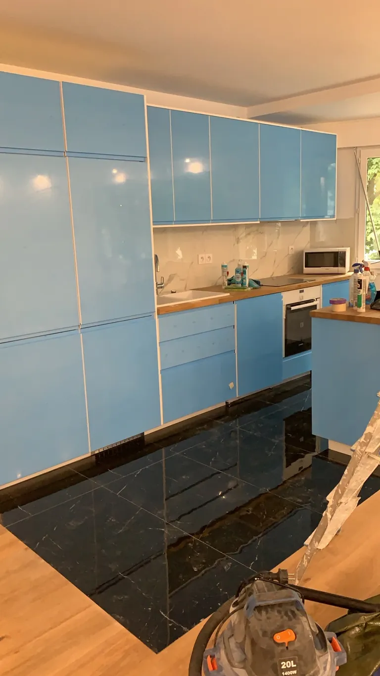 Cuisine en cours de pose avec protections bleues sur les façades, plan de travail aspect bois et sol carrelé noir veiné