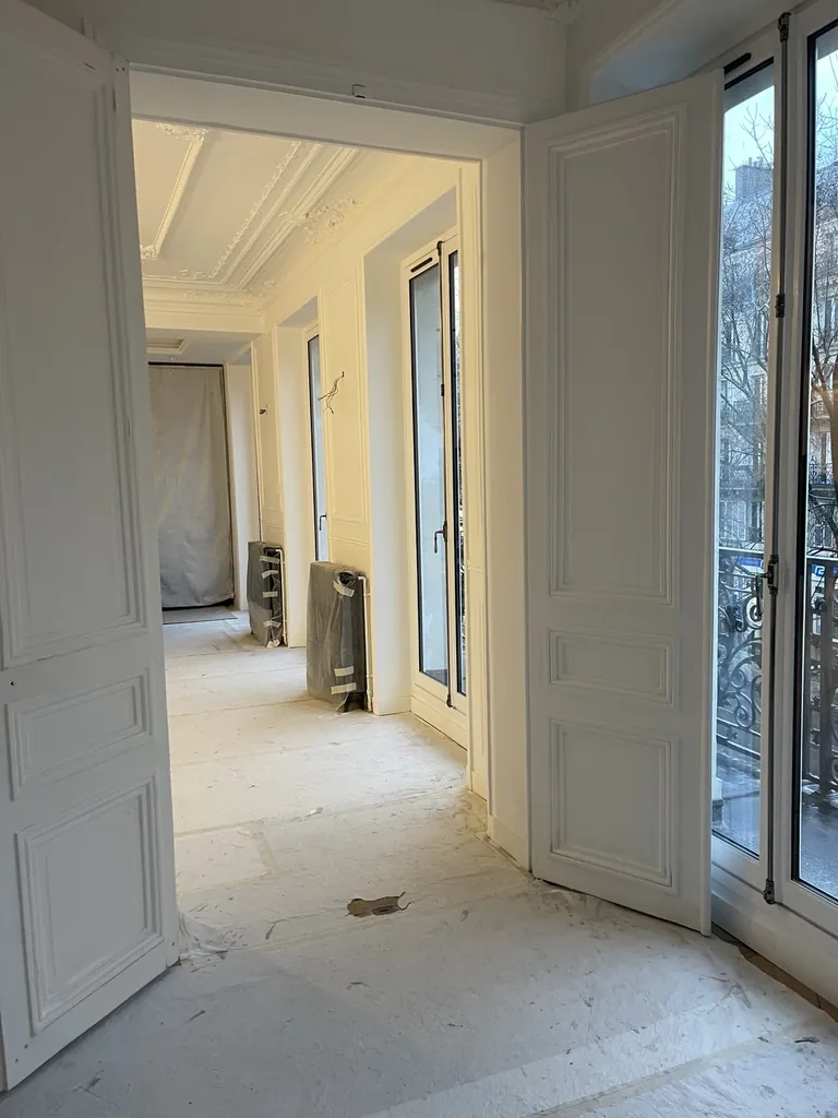 Enfilade de pièces en chantier avec portes moulurées, corniches, fenêtres blanches et sols protégés