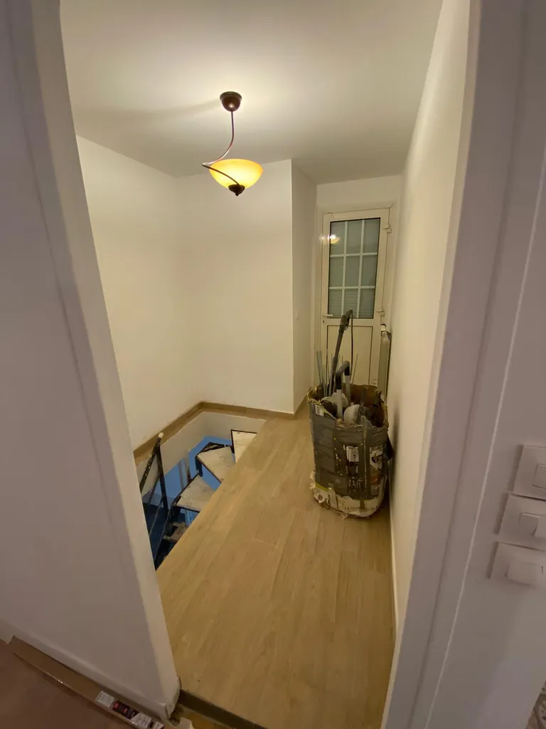 Palier en cours de finition avec murs blancs, sol aspect bois et trémie d’escalier