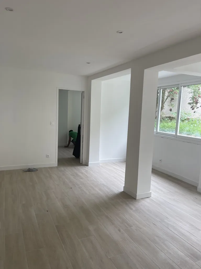 Pièce rénovée avec grandes ouvertures intérieures, murs blancs, spots et sol clair aspect bois