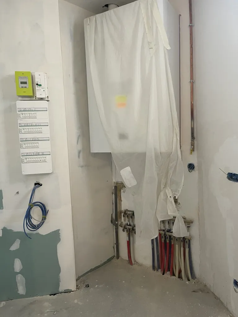 Tableau électrique, canalisations et collecteurs de plomberie dans un local en travaux