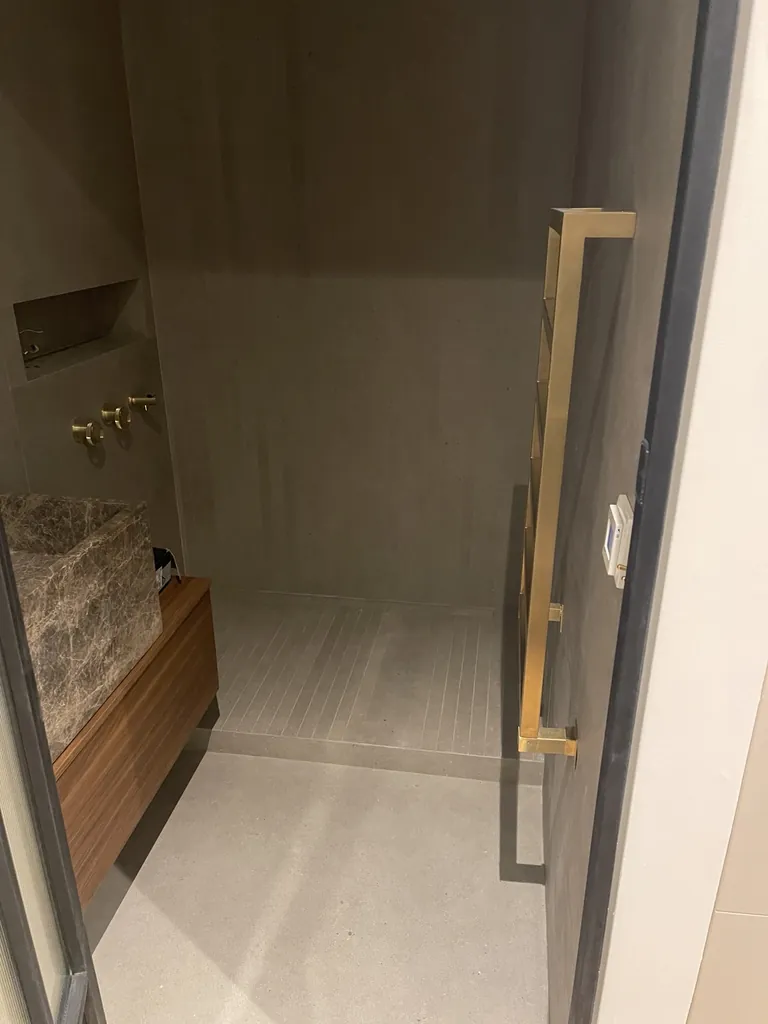Accès à une douche carrelée avec paroi vitrée, meuble vasque et revêtement de sol clair