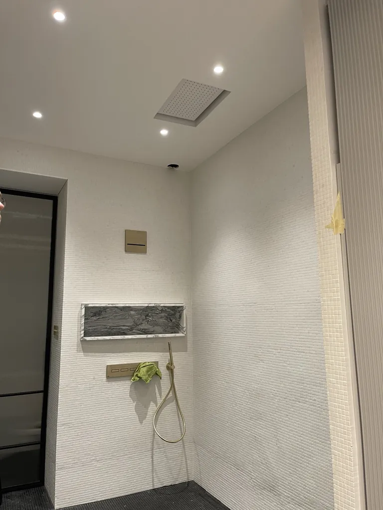 Douche avec mosaïque murale claire, niche veinée, robinetterie laiton et spots au plafond
